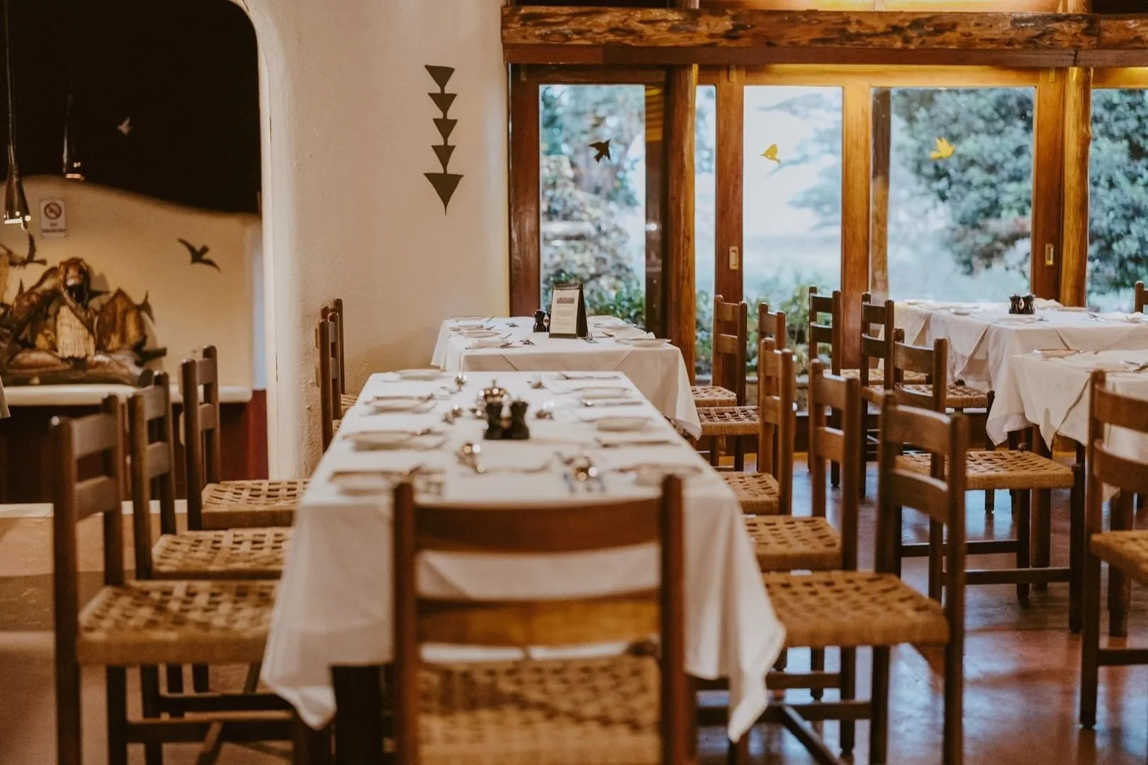 Tables set for dinner beneath wildlife murals, with garden views through the windows.
