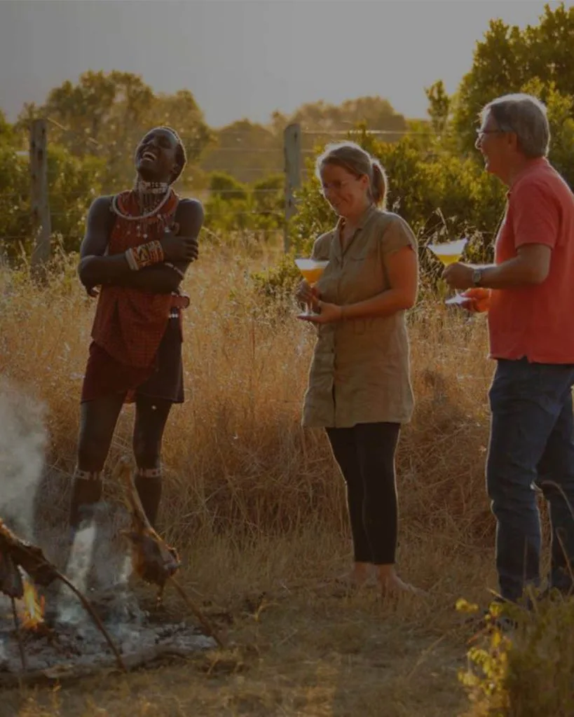 Guests enjoy sundowners around a campfire in the golden evening light of the Mara.