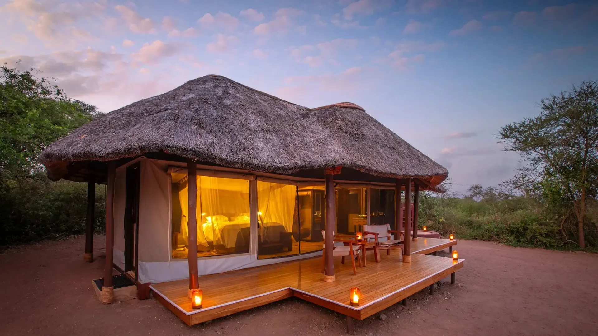 A guest tent's thatched exterior and private deck, set among the trees.