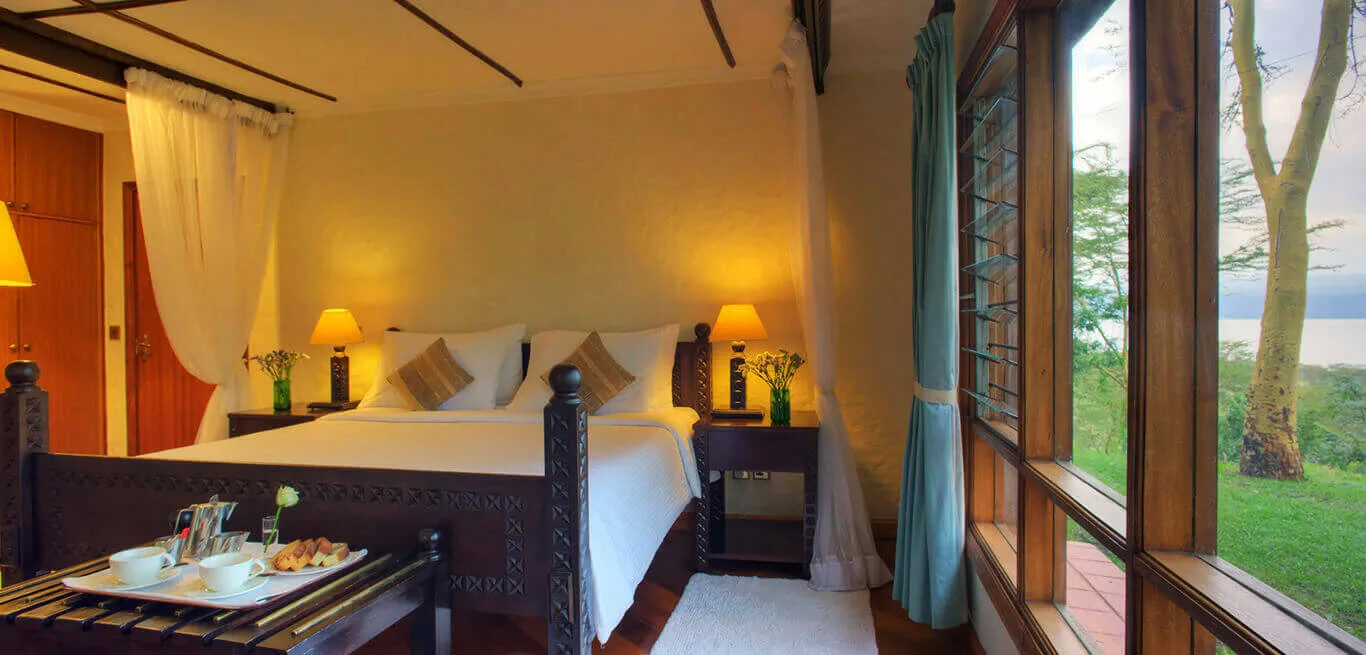 Rooms are furnished with hand-carved four-poster beds and views toward Lake Nakuru.