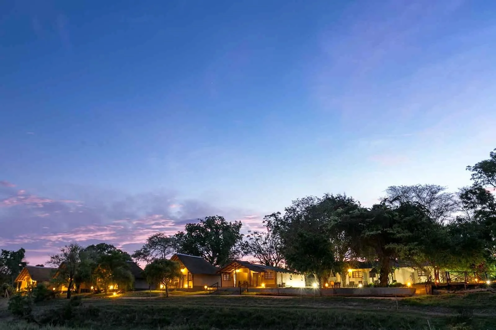 Umkumbe's thatched main lodge glows at dusk on the banks of the Sand River.