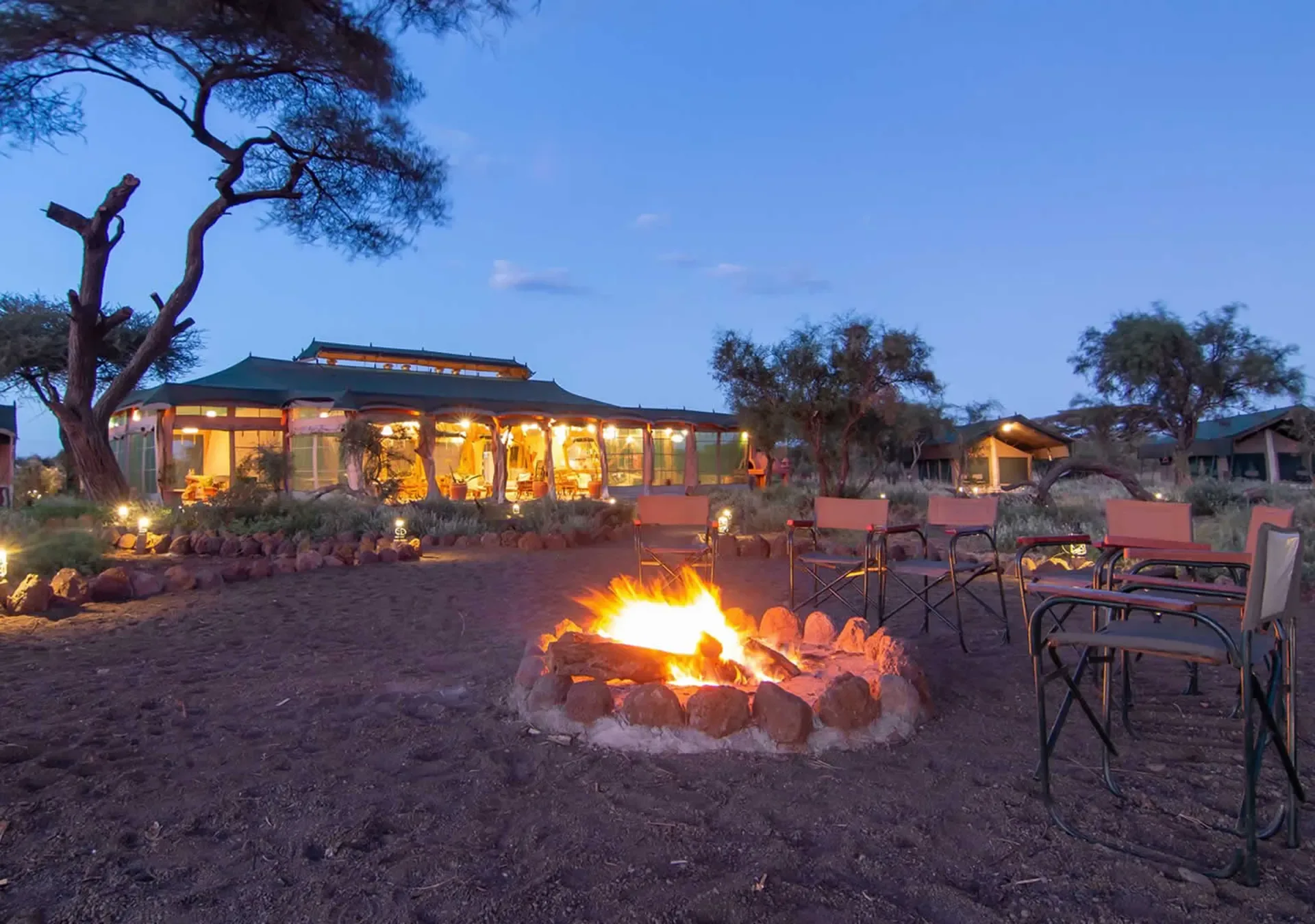 Evening falls at Amboseli Lodge, with the campfire lit and safari chairs waiting.