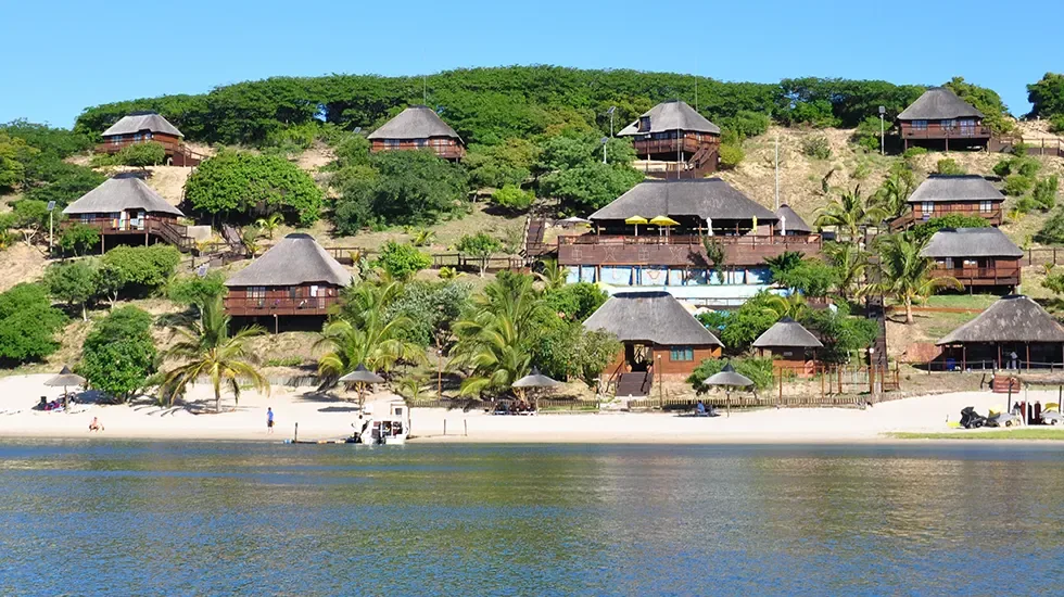 Thatched lodges above the white sand and calm water of Bilene, Mozambique.