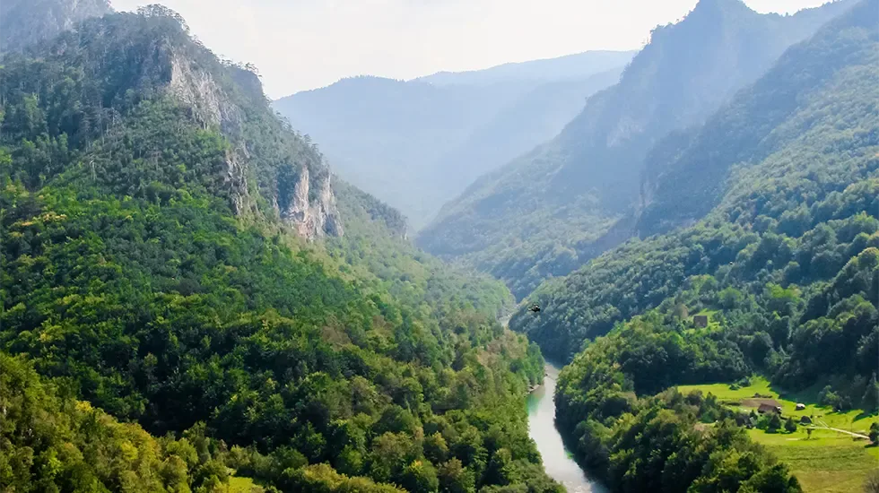 A green river valley winds between forested hills in the Great Rift Valley.
