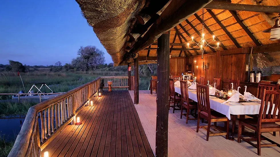 Lantern-lit dining deck at Gunns Camp, Botswana, overlooking the Delta at dusk.