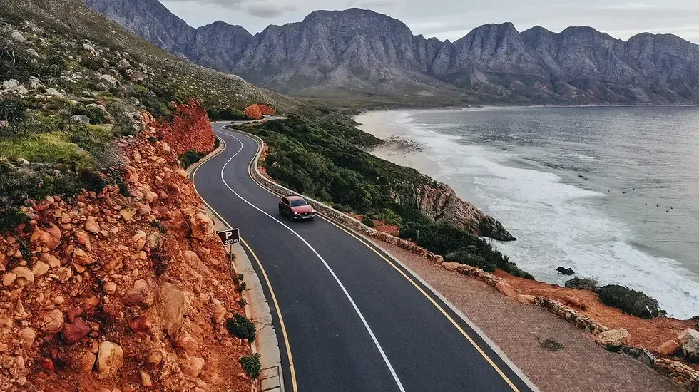 A coastal drive towards Hermanus, with mountains and ocean alongside the road.