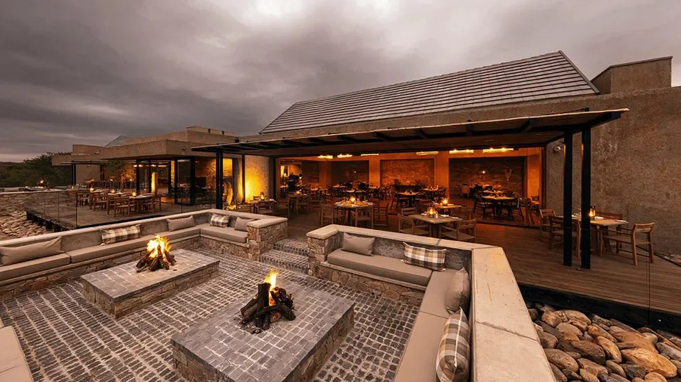 Fire pits and cushioned seating at a Kapama lodge in South Africa as evening falls.
