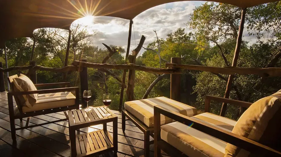 Two glasses of wine on a Kapama lodge deck as the sun sets over the bushveld.