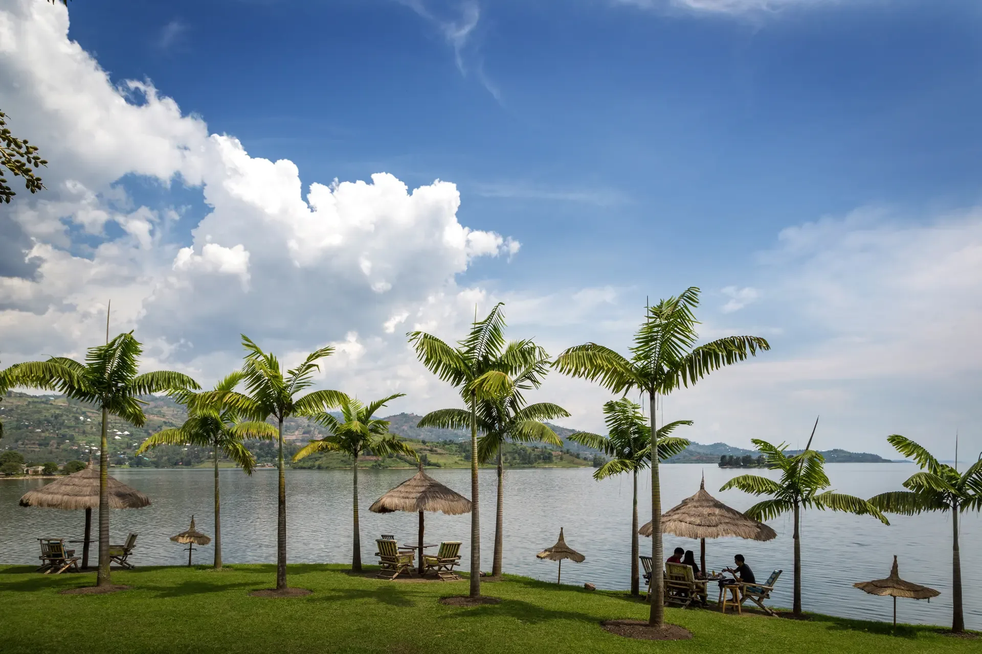 Guests relax under thatched parasols on the green shore of Lake Kivu, Rwanda.
