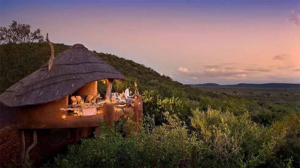 Dinner laid out under a thatched roof at dusk in Madikwe Private Reserve, South Africa.