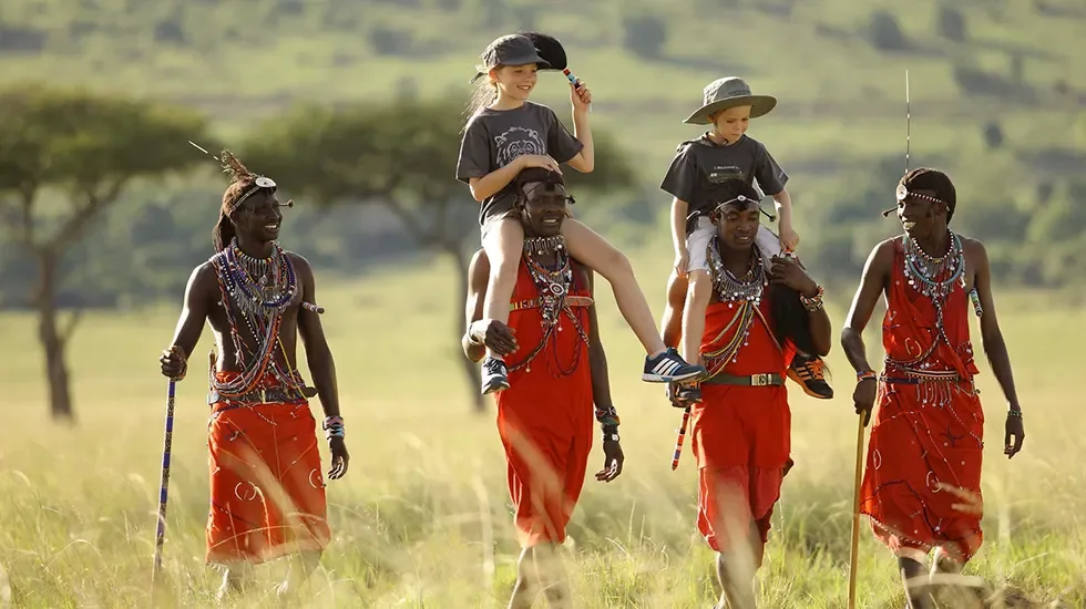 Maasai warriors carry two young visitors through the tall grass of the Masai Mara.