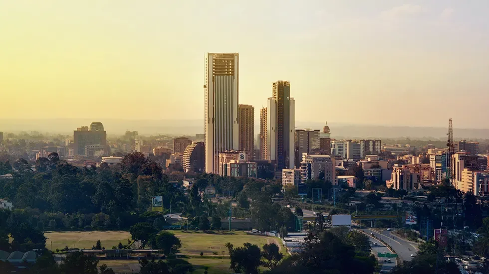 Nairobi's skyline at golden hour, seen across green parkland and city trees.