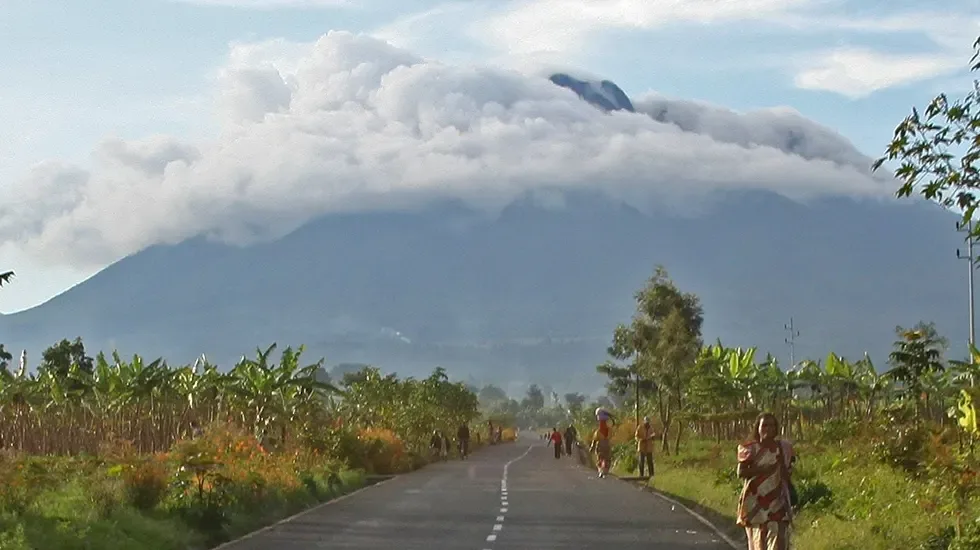 A road through banana plants near Volcanoes National Park, Rwanda, with a volcano under cloud.