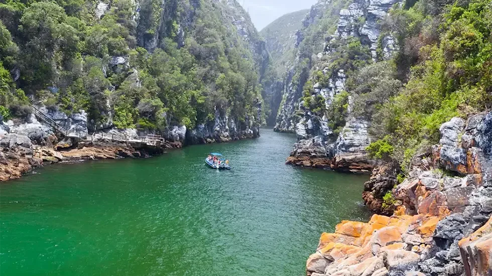 A boat glides through the green water of the Storms River gorge in Tsitsikamma National Park.