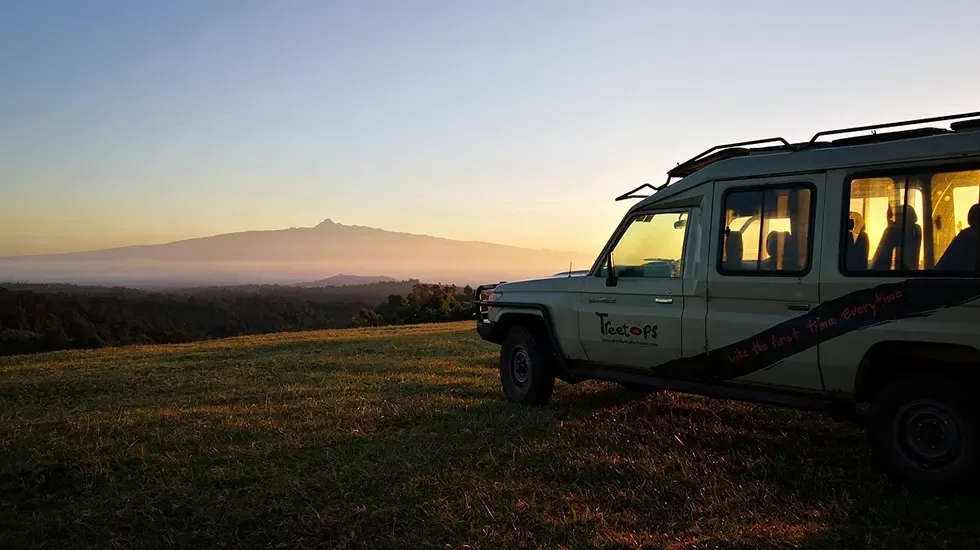 A safari vehicle waits on the grass at Treetops as the sun sets over the horizon.