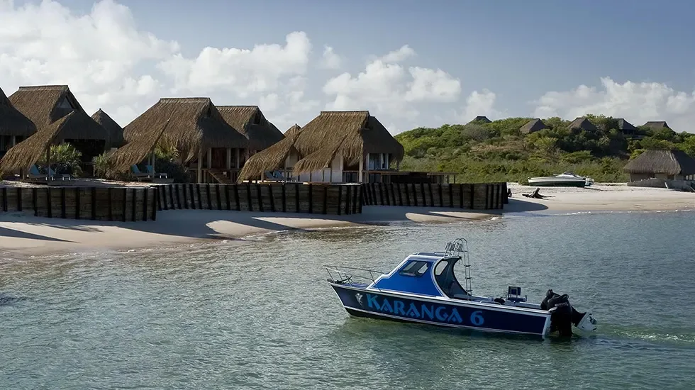 A boat idles off the beach at Vilanculos, Mozambique, where thatched lodges face calm lagoon water.