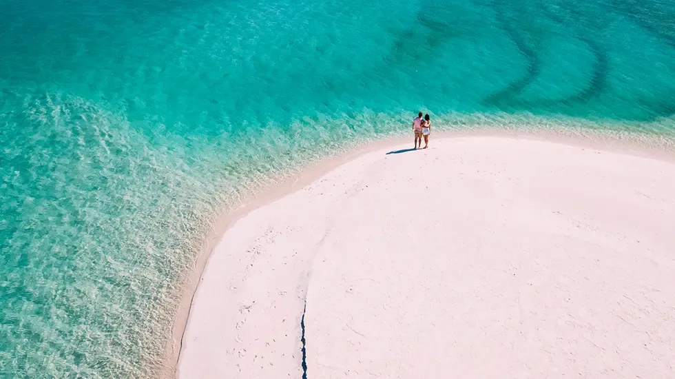 Two travellers on a pale sandbank beside clear turquoise water in Vilanculos, Mozambique.