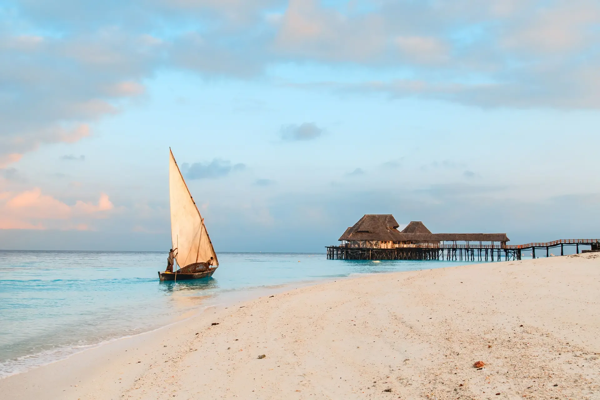A dhow under full sail off the white sands of Zanzibar at sunset.