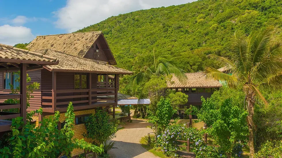 Timber lodge buildings with tiled roofs and balconies among palms and flowering shrubs