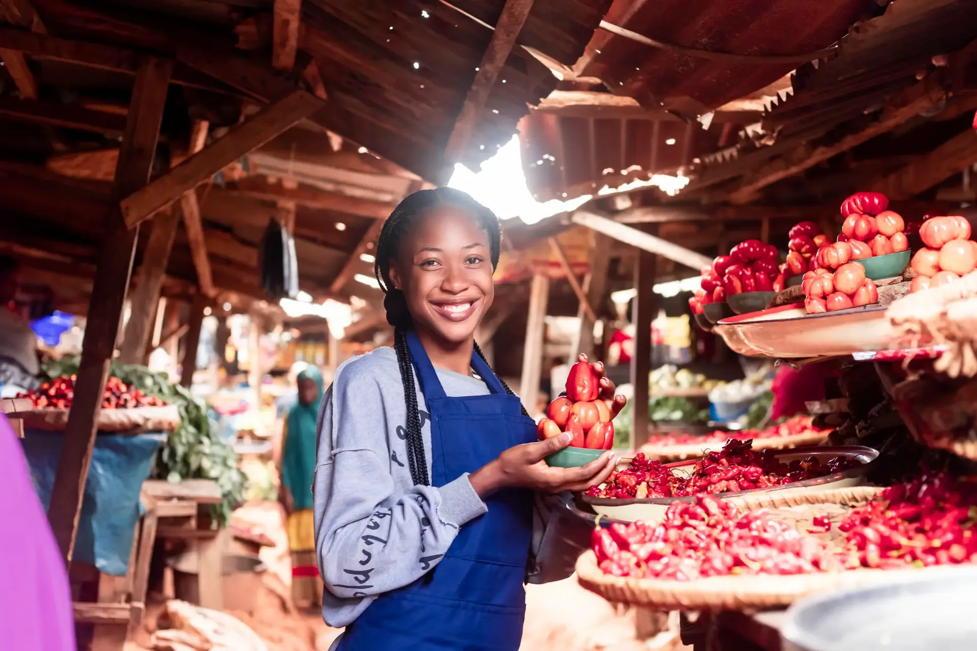 A market trader in a colourful apron selling tomatoes and vegetables at a local market