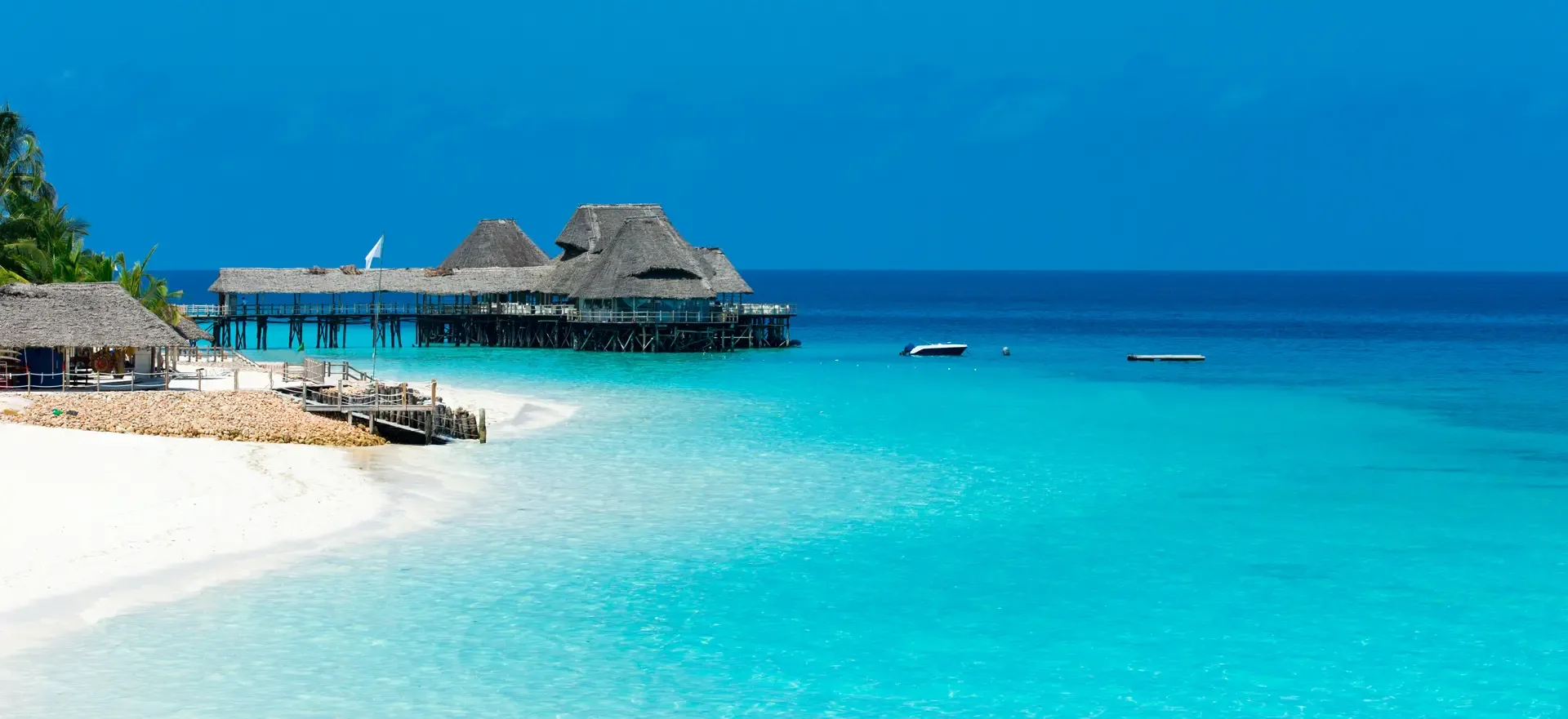 Turquoise water and white sand at Zanzibar, with thatched buildings on stilts over the sea.