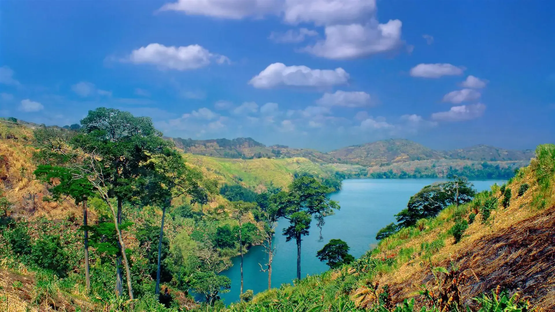 A crater lake near Fort Portal, Uganda, ringed by green hills and tall trees.