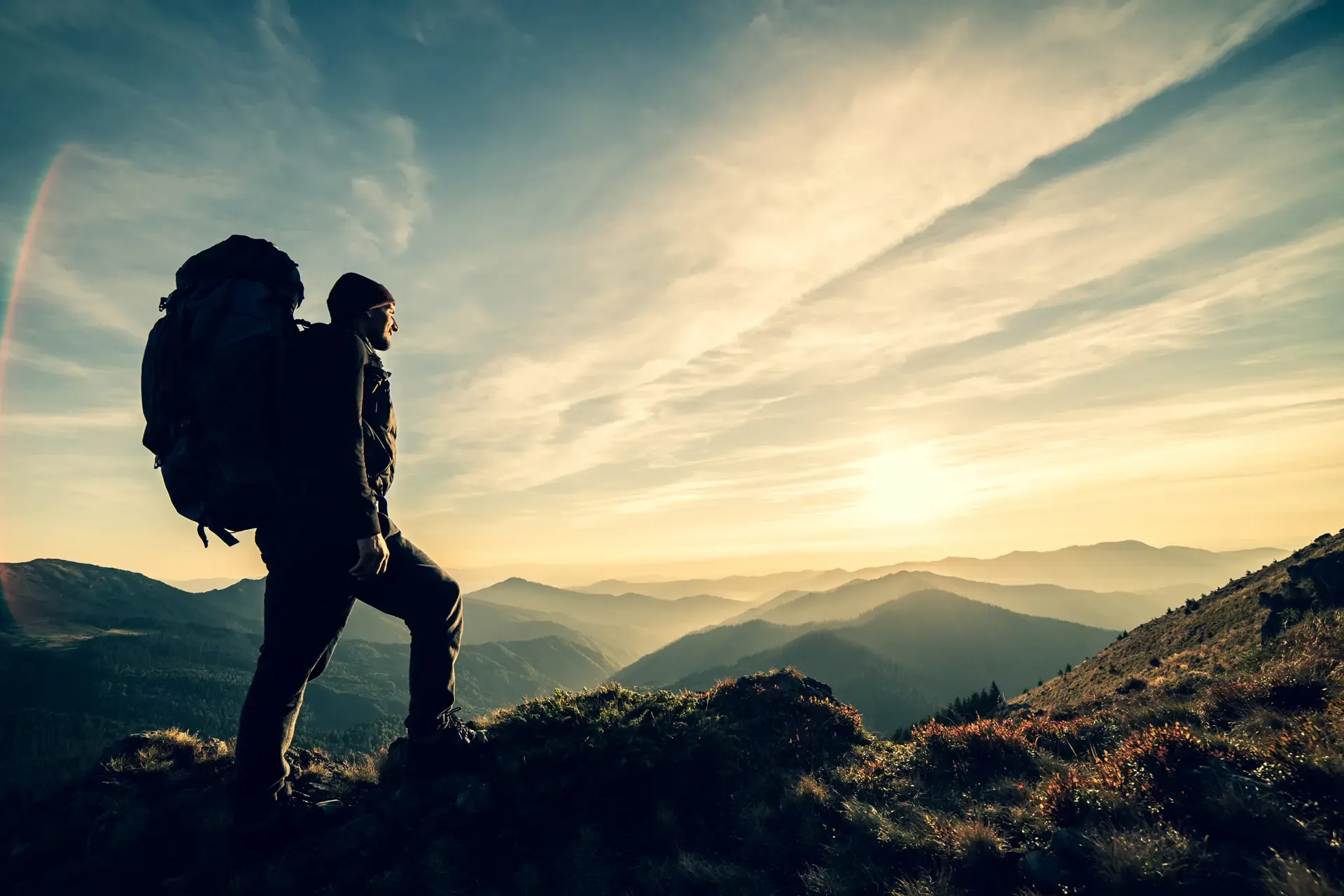 Man standing with camping backpack rock with picturesque sunset