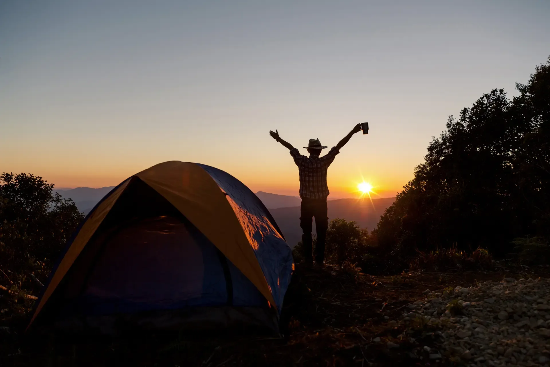 Silhouette happy man with holding coffee cup stay near tent around mountains