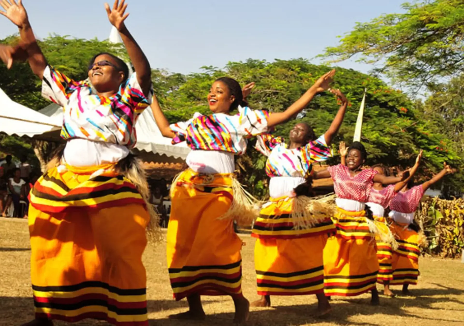 Dancers in bright traditional dress perform outdoors in Uganda.