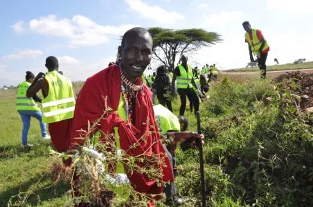 A Maasai man in a red shuka clearing scrub alongside a crew in high-visibility vests during a habitat restoration day