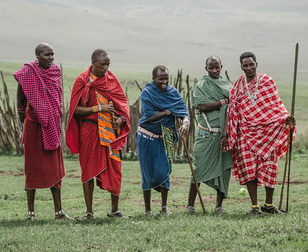 Five Maasai men in patterned shukas standing together on the grass of the Ngorongoro highlands