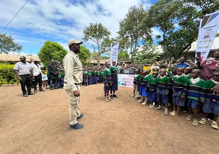A Gosheni staff member addressing rows of uniformed pupils in a school yard
